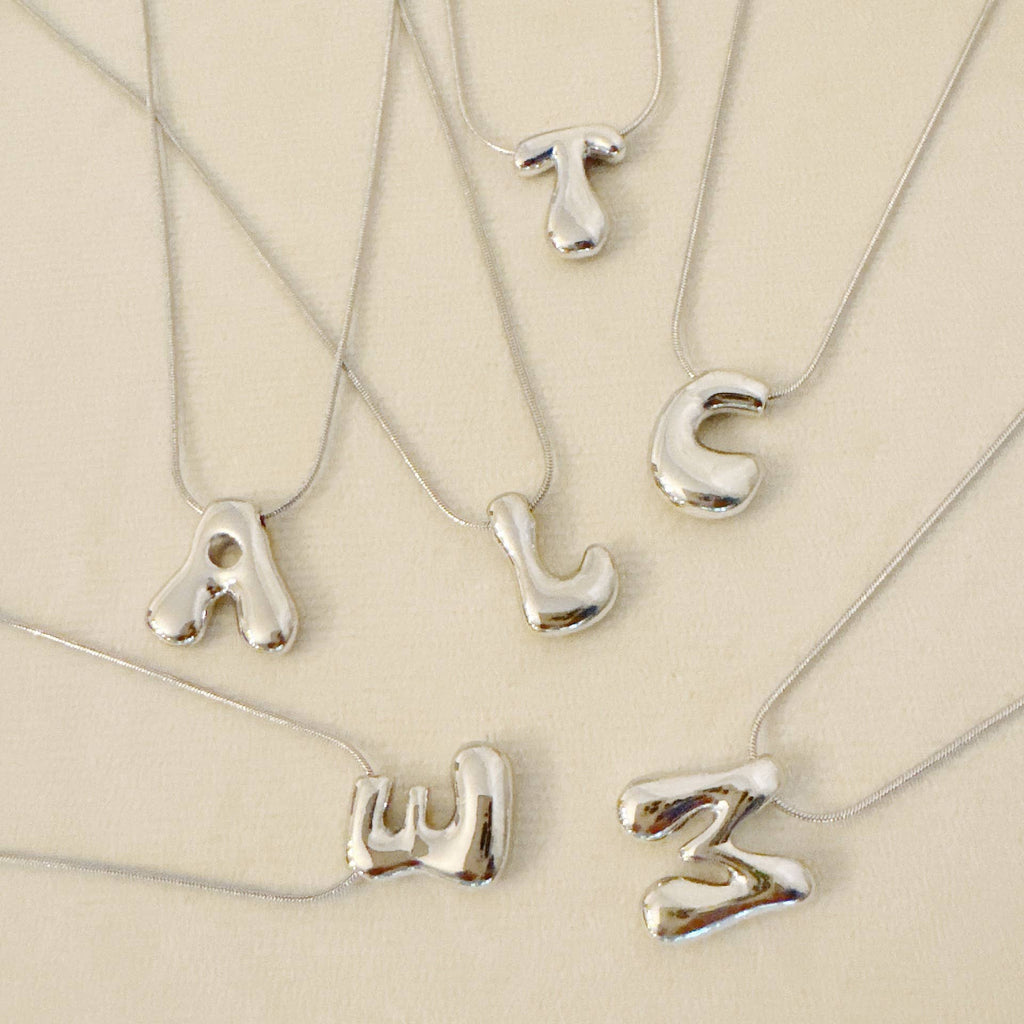 A collection of silver initial necklaces in a bubble font.