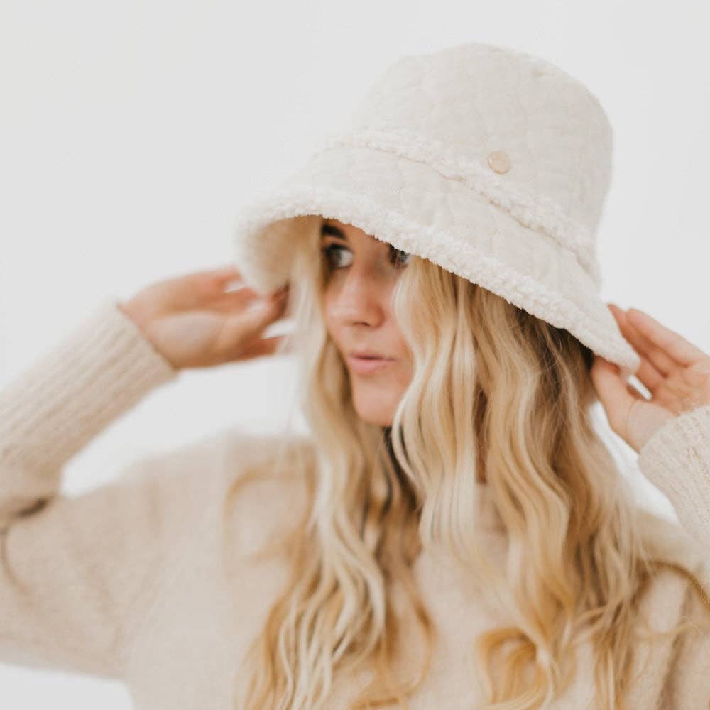 Woman wearing a beige knit hat and sweater against a white background