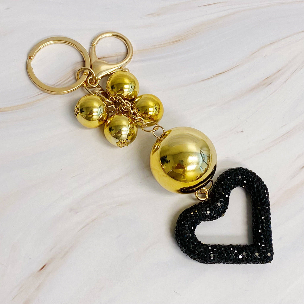 A gold-colored key chain featuring a series of round baubles with a black heart-shaped charms with rhinestone embellishments.