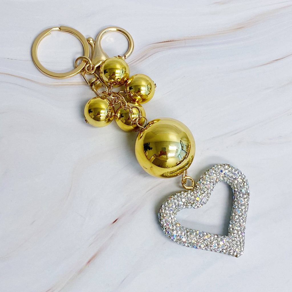 A gold-colored key chain featuring a series of round baubles with a silver heart-shaped charm with rhinestone embellishments.