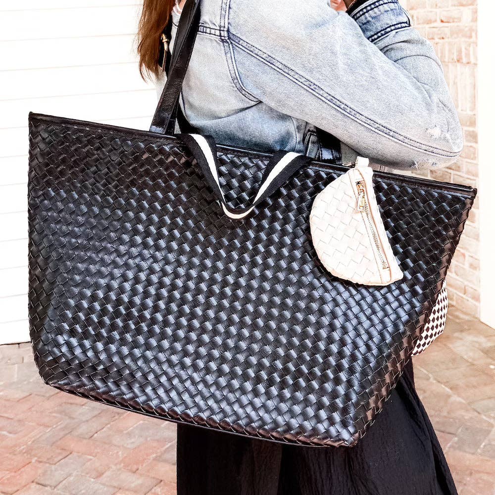 Person holding a large black woven handbag with a mini zippered charm bag
