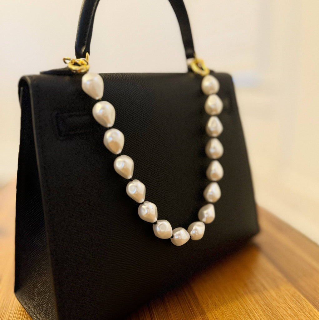 A black bag with a pearl and bead bag charm attached , featuring a gold plated clasp