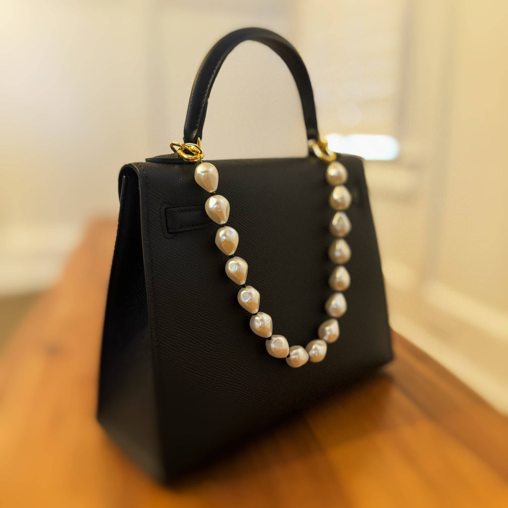 A black bag with a pearl and bead bag charm attached , featuring a gold plated clasp