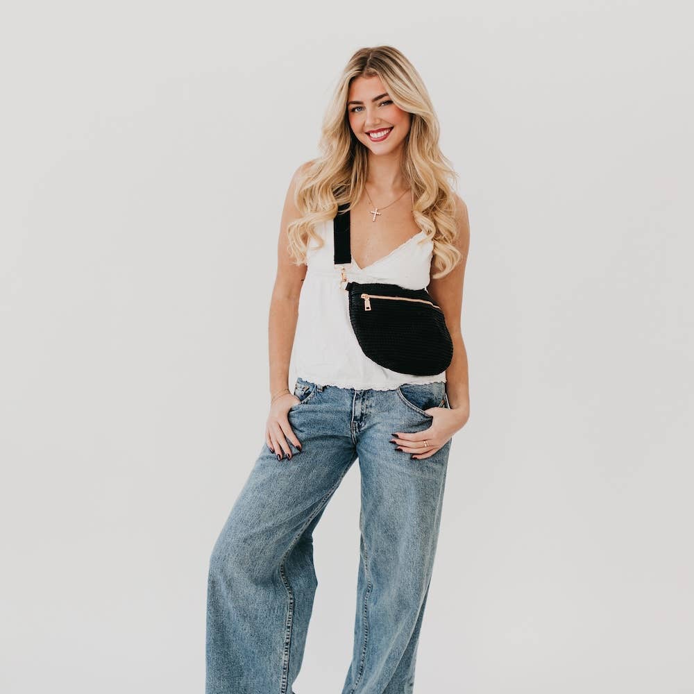 A person wearing black raffia bum bag with a gold zipper and adjustable strap.