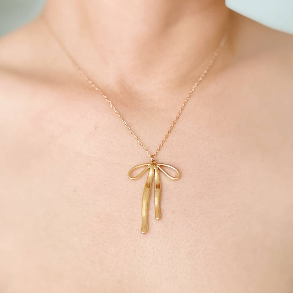 Gold necklace with a delicate bow pendant on a person's neck