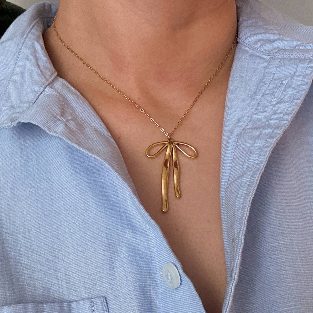 Gold necklace with a bow pendant worn by a person in a light blue shirt.