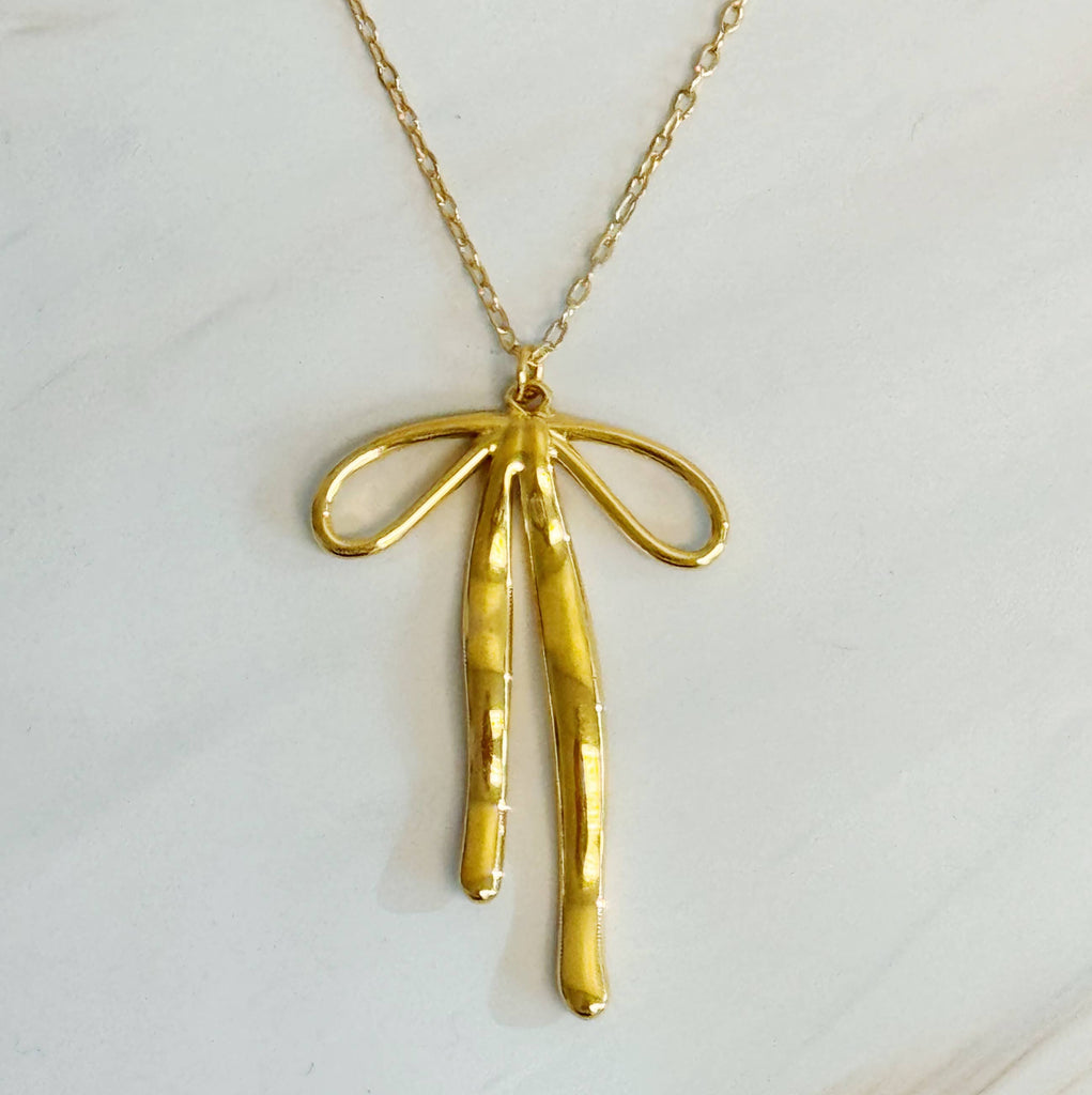 Gold bow-shaped pendant on a chain against a light gray background