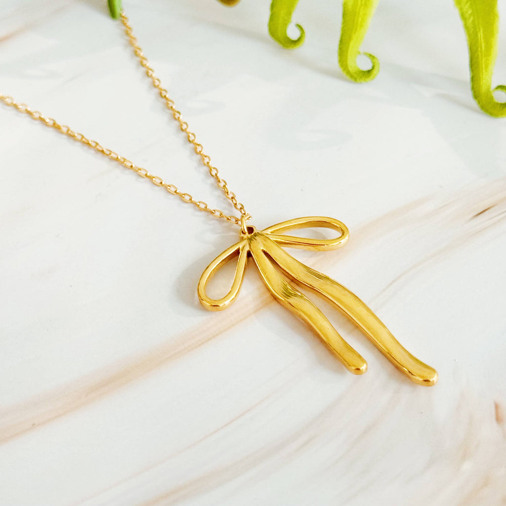 Gold bow-shaped pendant necklace on a light surface
